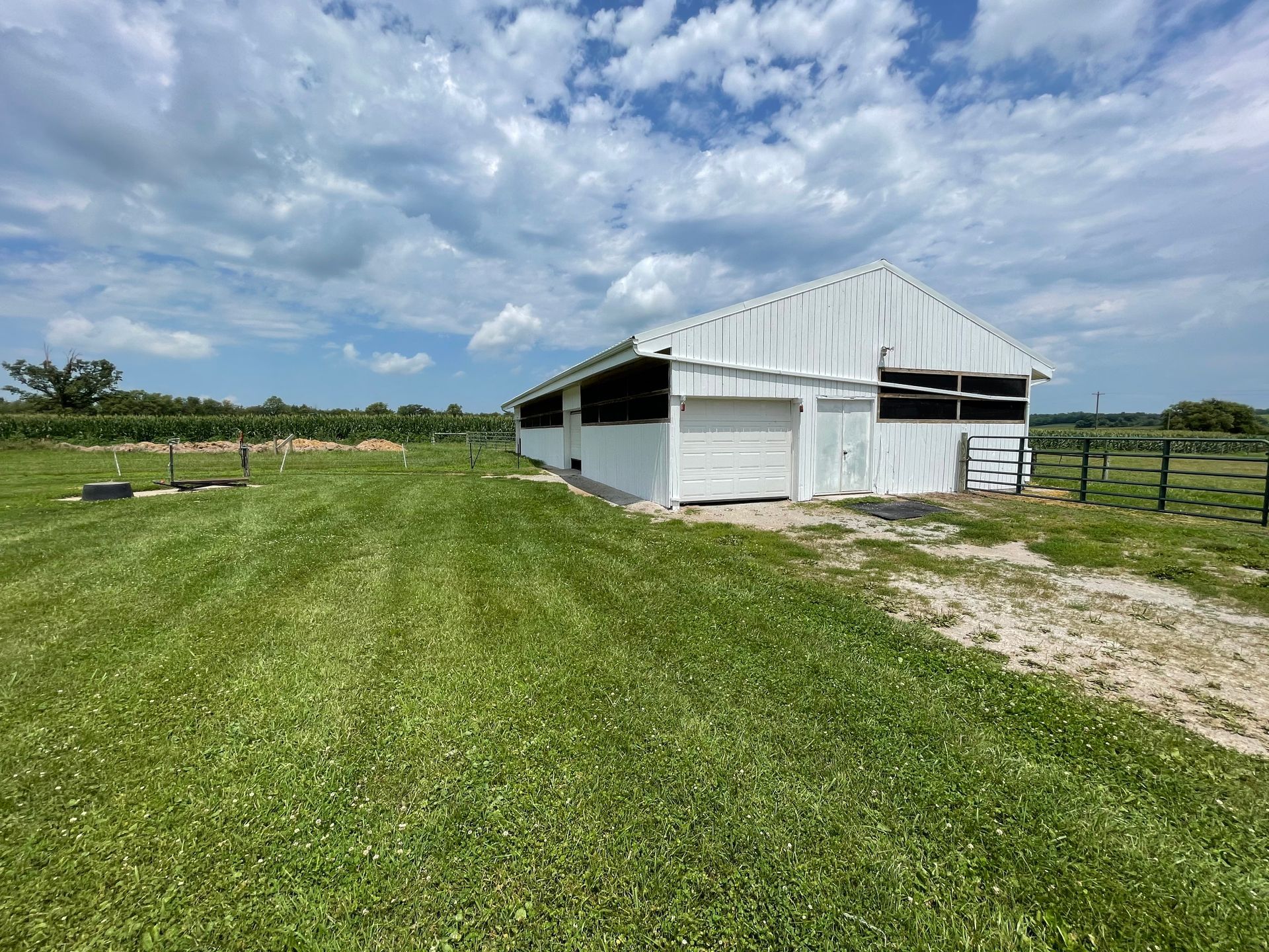 A white barn is sitting in the middle of a grassy field.