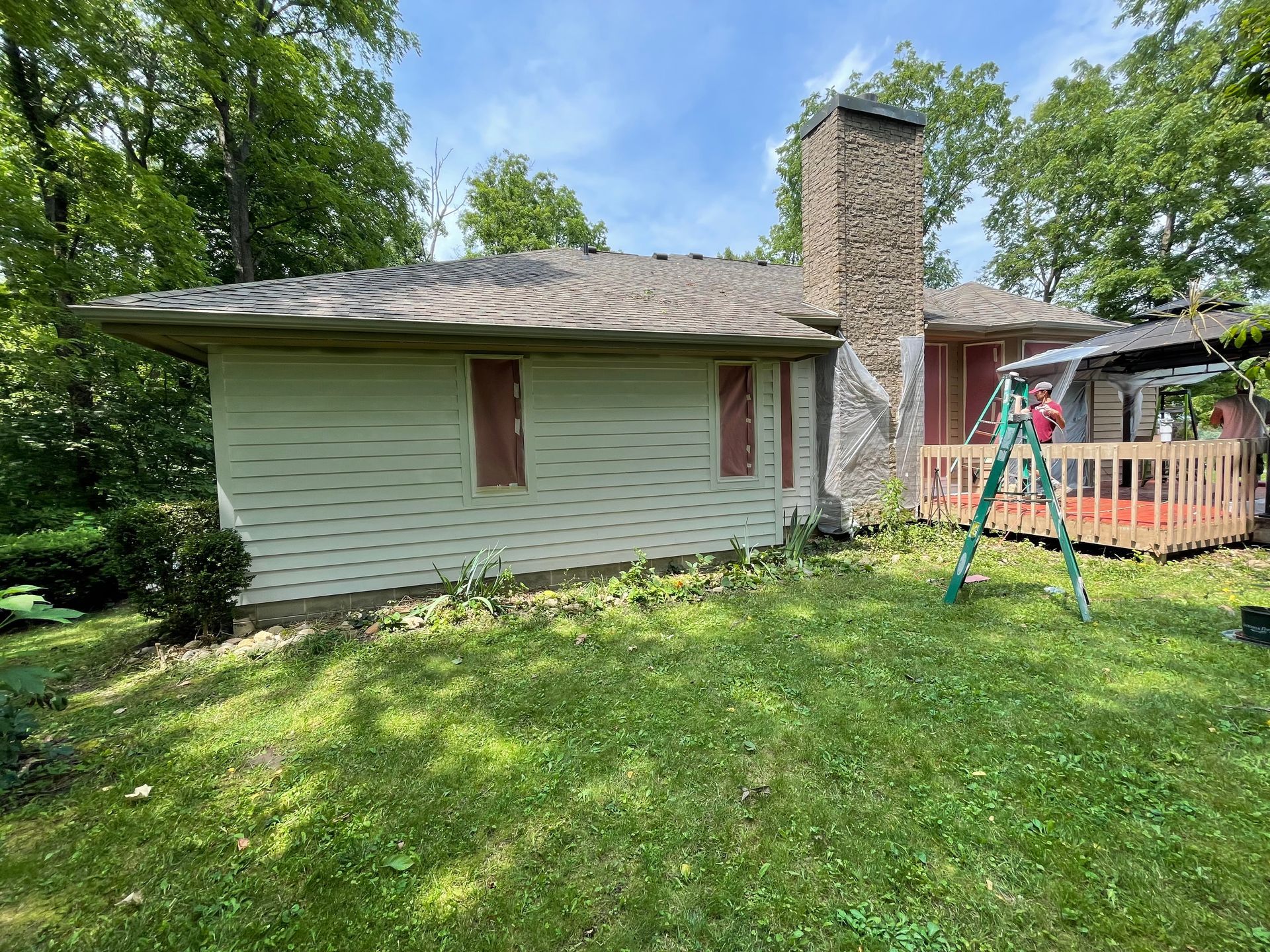 A house with a ladder in front of it is sitting on top of a lush green lawn.