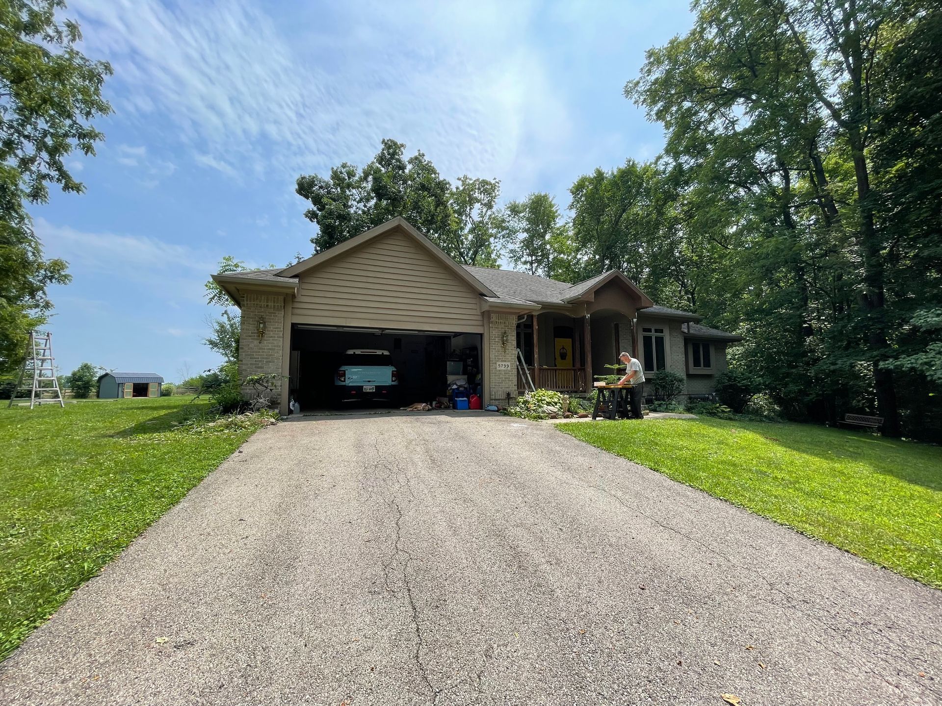 A house with a car parked in the garage and a gravel driveway leading to it.