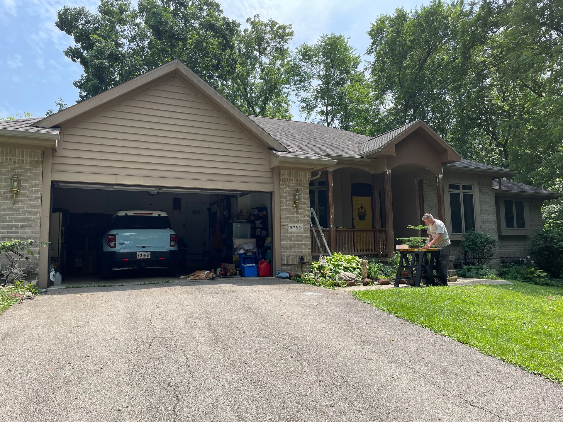 A man is standing in front of a house with a car in the garage.