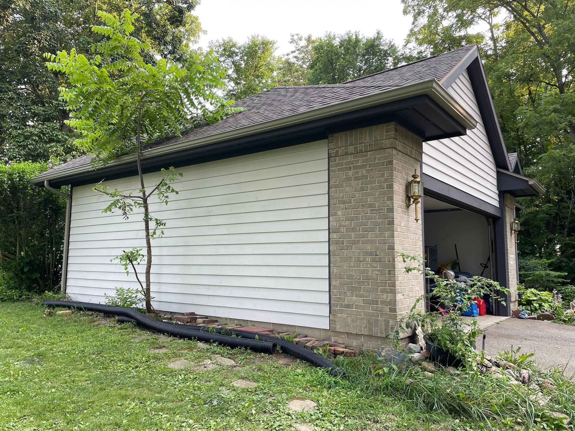 A white garage with a black roof is sitting in the middle of a lush green field.