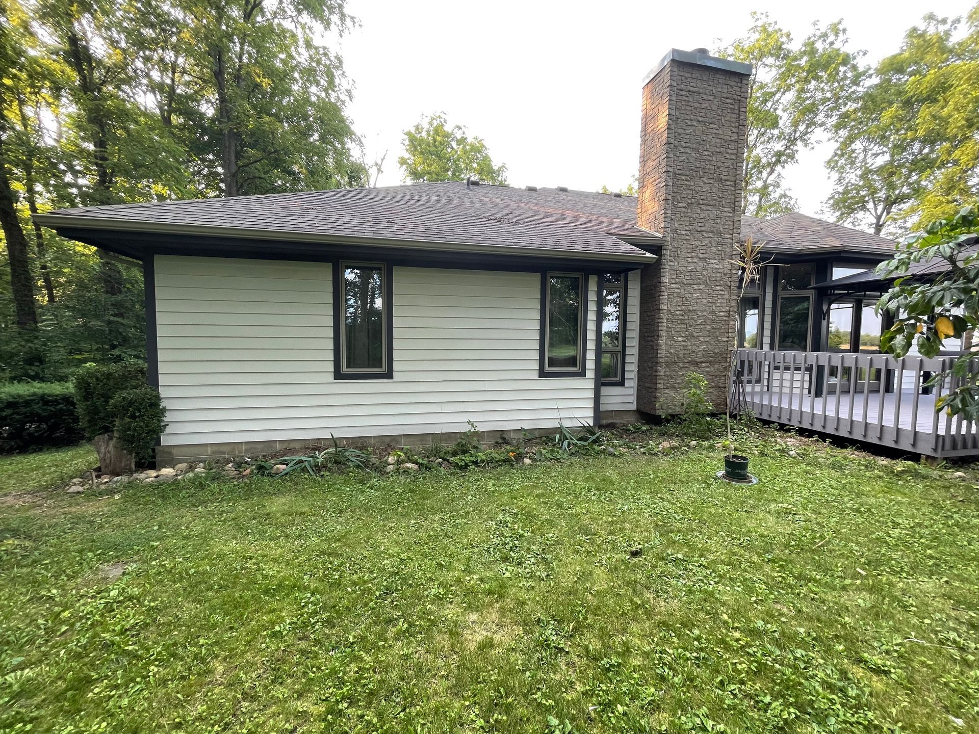 A white house with a stone chimney and a deck in the backyard.