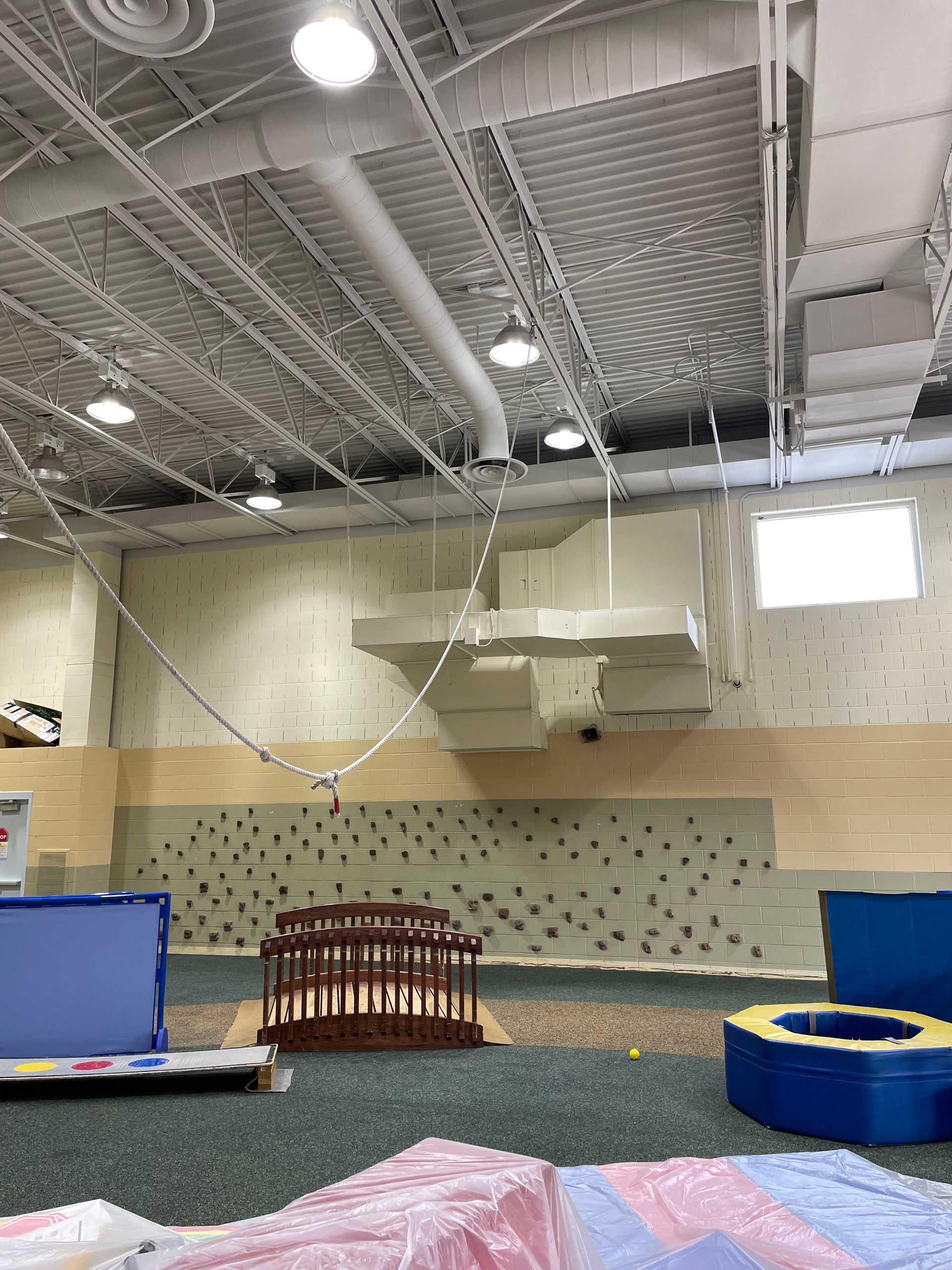 A large indoor gym with a climbing wall and a trampoline.