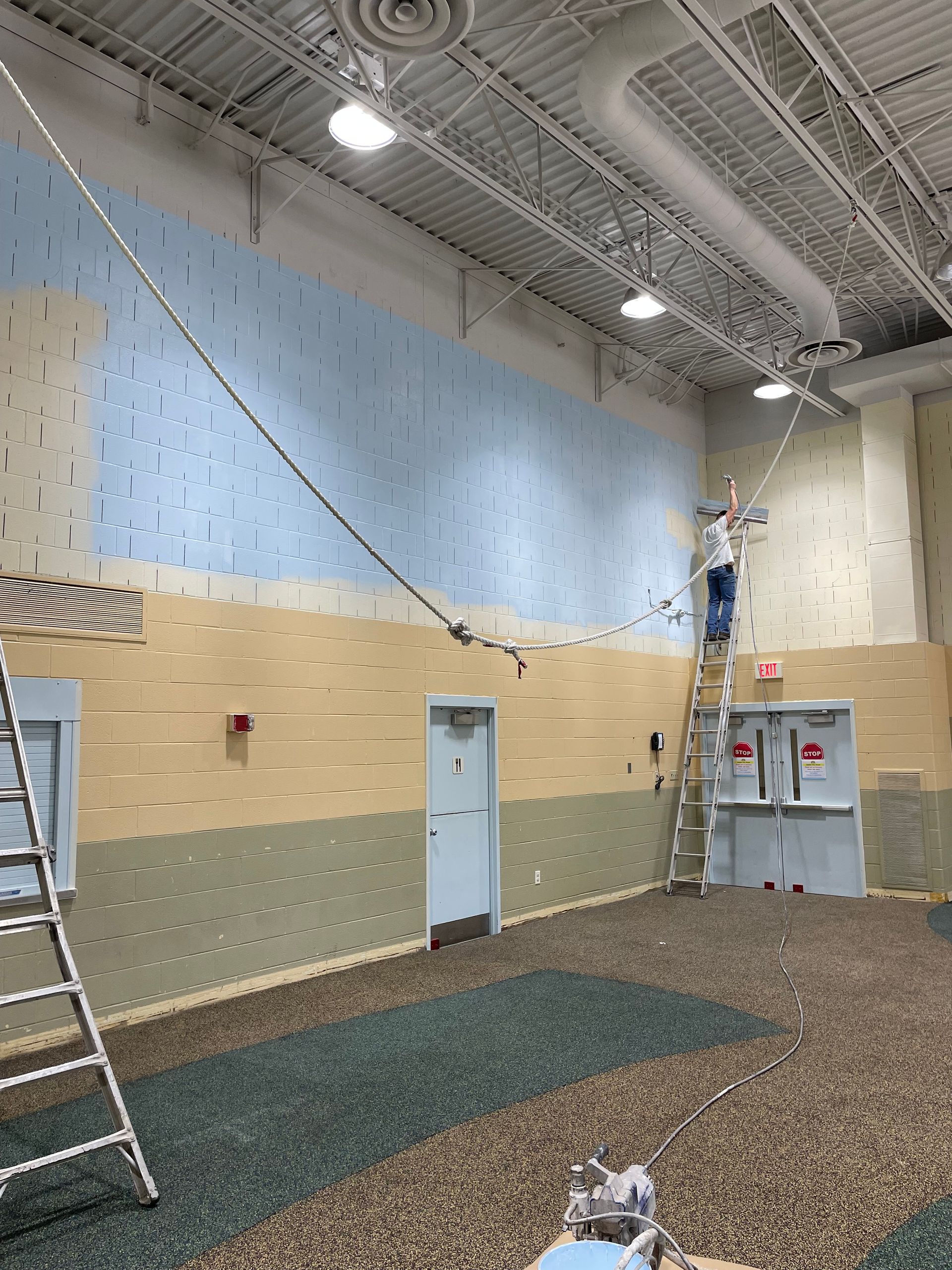 A man is standing on a ladder painting a wall in a building.
