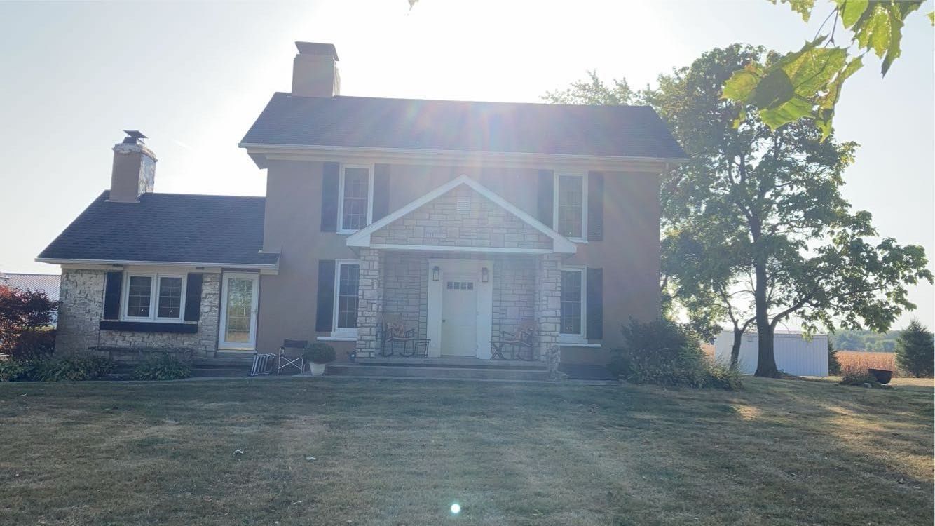 A large brick house with a black roof is sitting on top of a grassy hill.