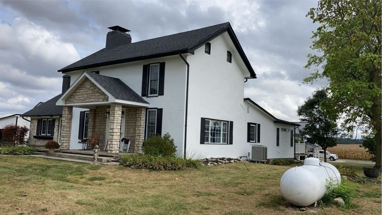 A white house with black shutters and a propane tank in front of it