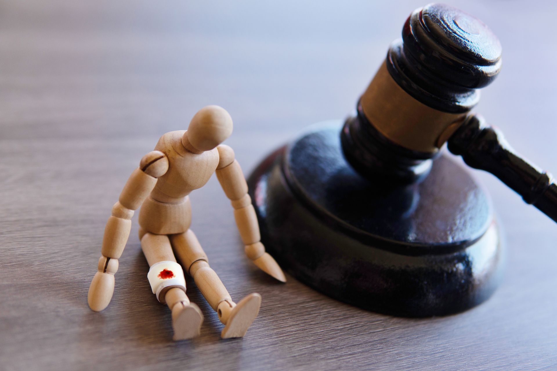 Wooden figure beside a judge’s gavel, one leg bandaged, symbolizing injury and legal judgment