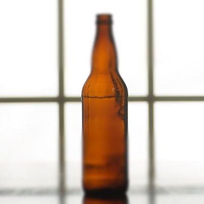 A bottle of beer is sitting on a table in front of a window.