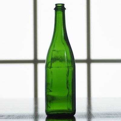 An empty green bottle sits on a table in front of a window