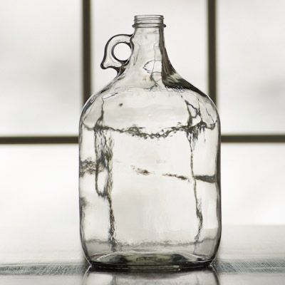 An empty glass bottle with a handle is sitting on a table.