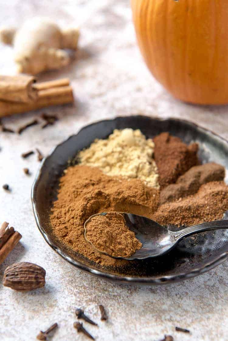 A plate of spices with a spoon in it and a pumpkin in the background.