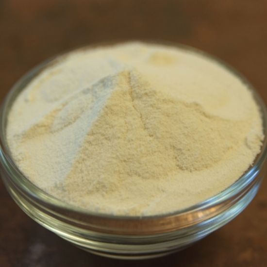 Small glass bowl filled with pale yellow powder on a wooden surface
