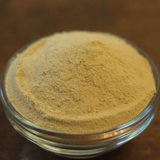 Bowl of pale beige powder on a wooden surface, close-up.