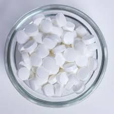 A glass bowl filled with white pills on a white surface.