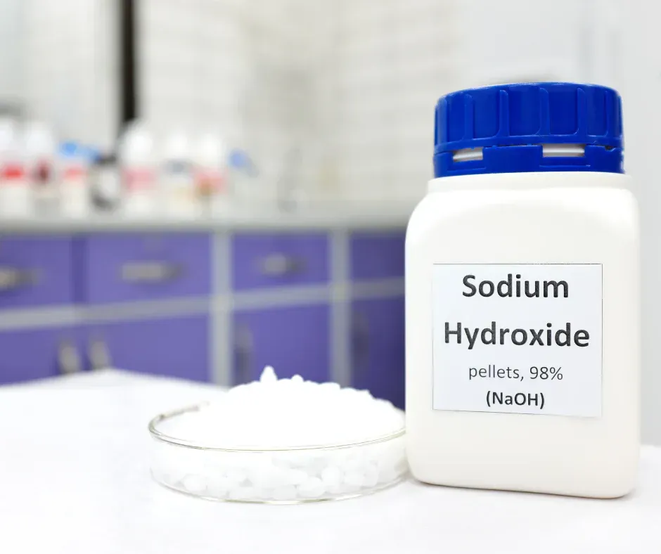 A bottle of sodium hydroxide is sitting on a table next to a pile of sodium hydroxide.
