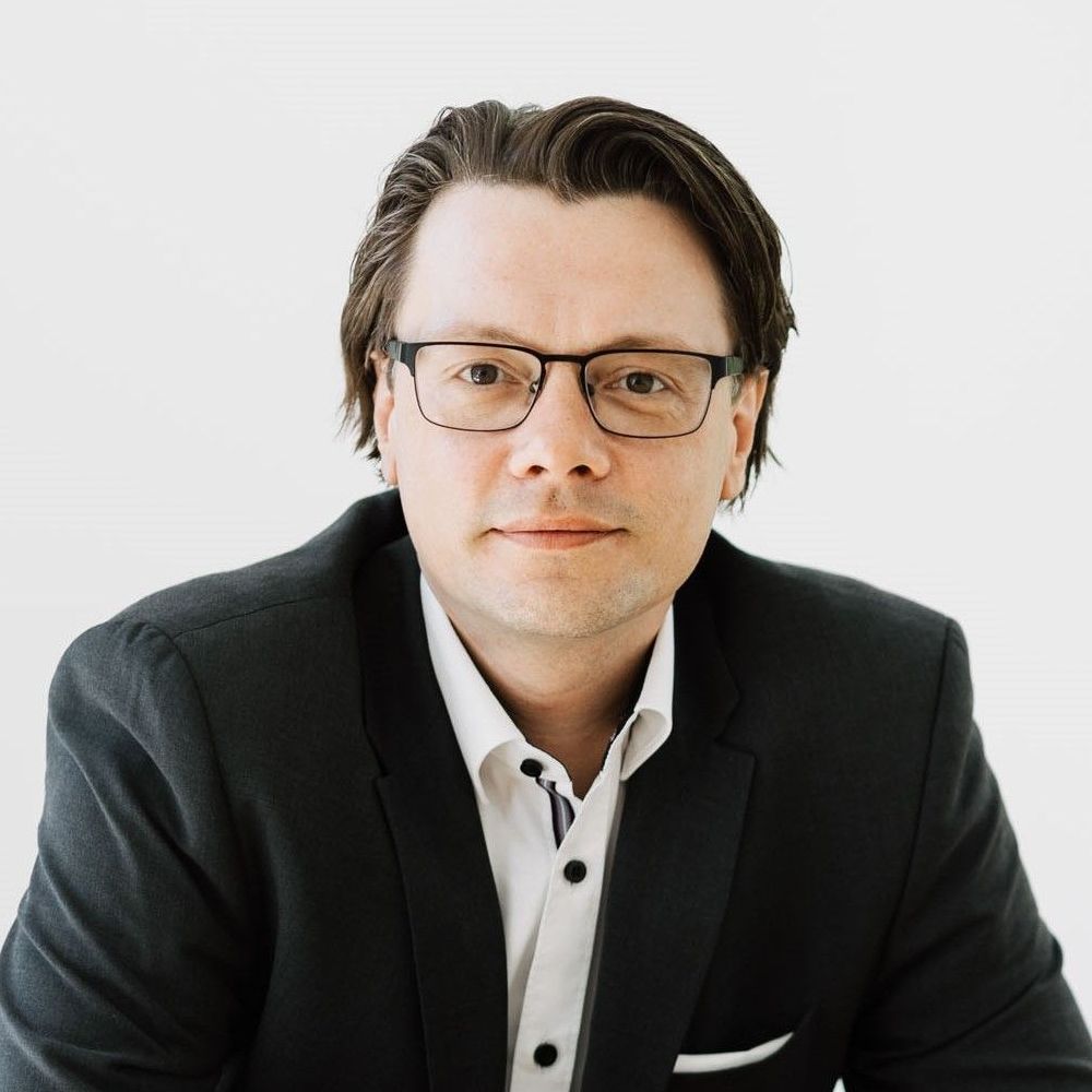 Porträt von Alexander Kukovic - Finanzberater. Das Bild zeigt ihn im Anzug am Tisch, freundlich und kompetent im Blick.