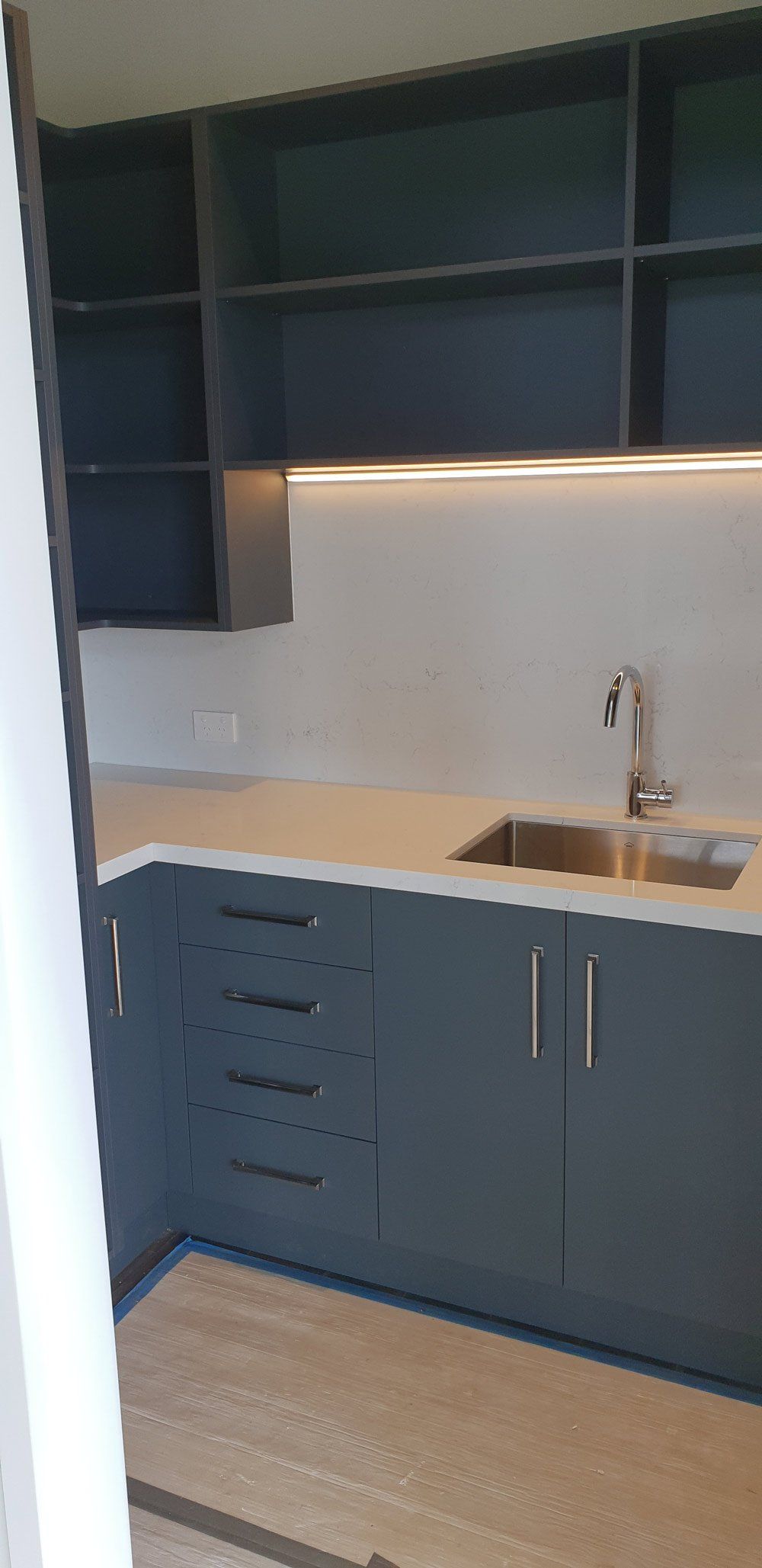 Blue kitchen cabinets with white countertop, sink, and open shelving under warm under-cabinet lighting — Bespoke Kitchens in Balaclava NSW