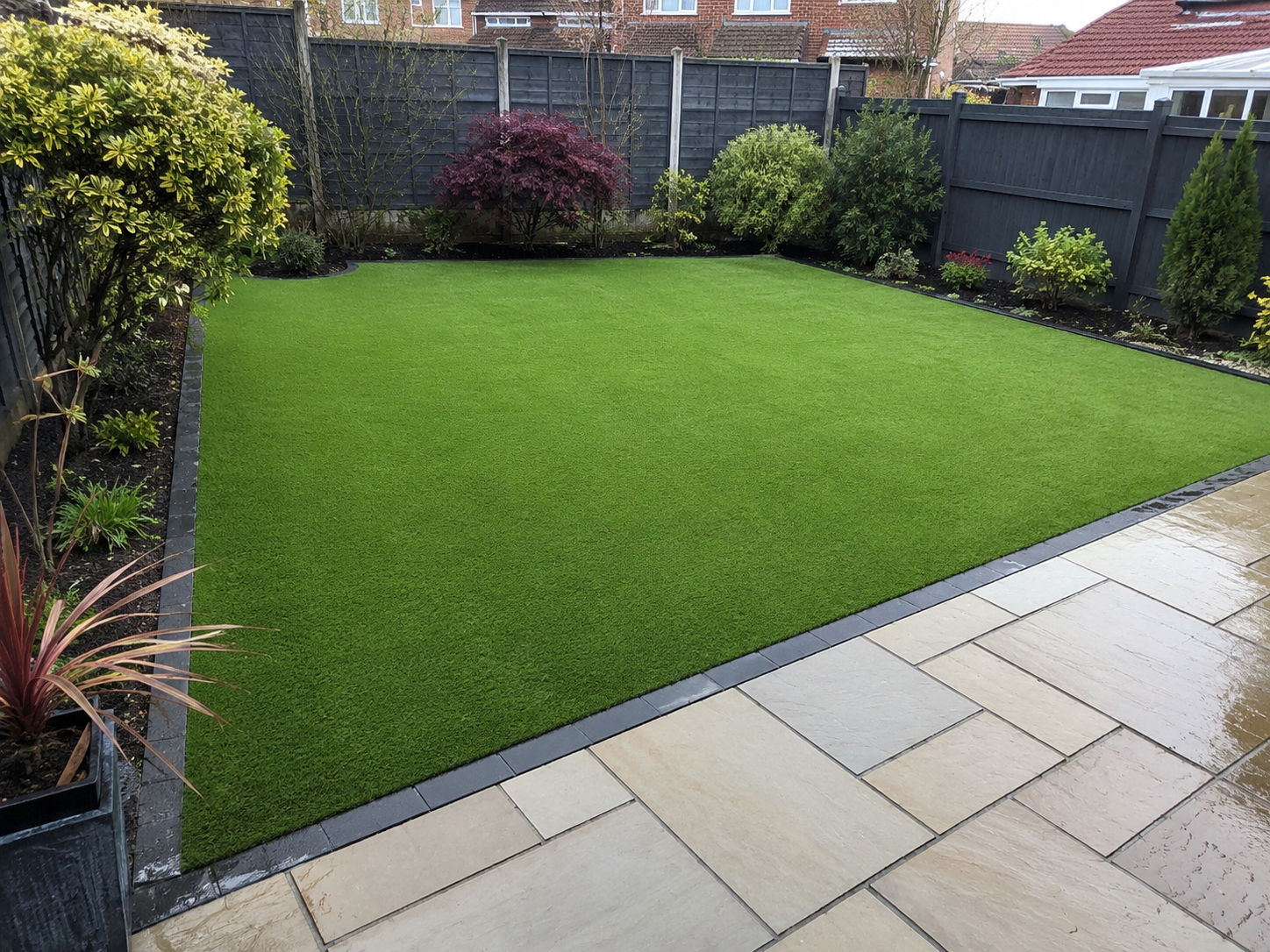 Well-kept green lawn with concrete path, wooden fence, and tall trees in a suburban backyard