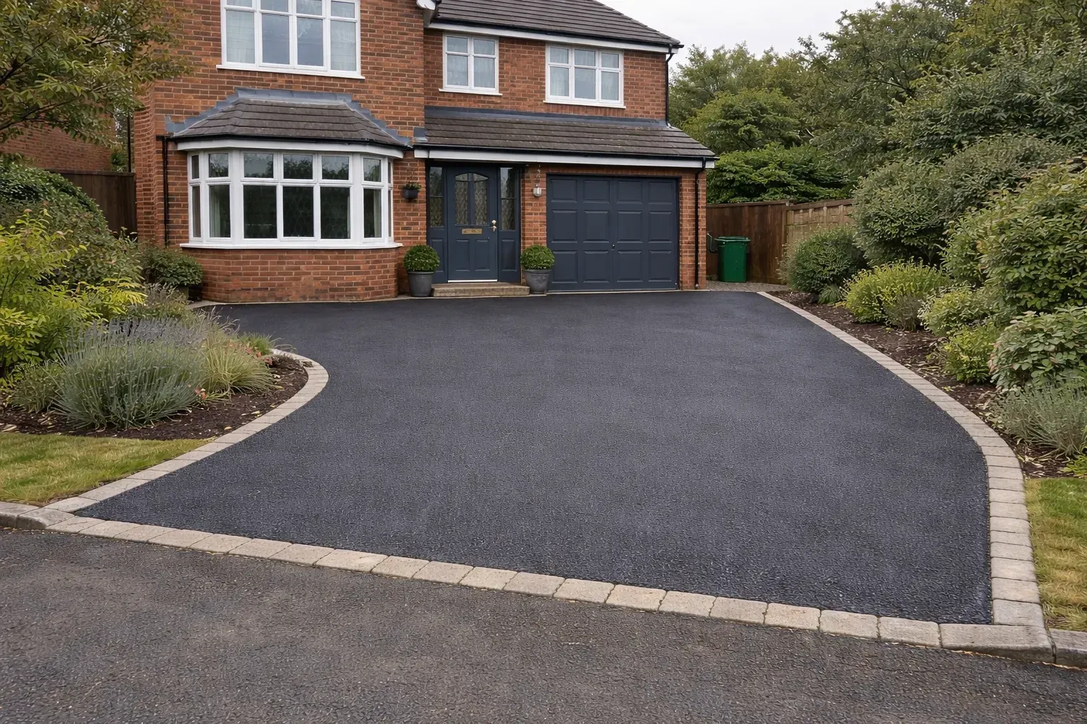 Curved black driveway leading to a brick house with a garage and landscaped shrubs