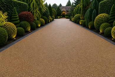 Resin driveway lined with manicured bushes and trees, leading to a stone house. 