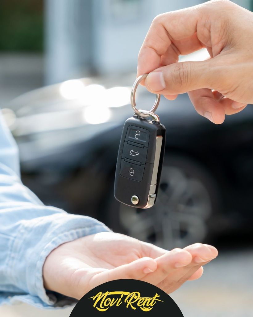 Porgere il telecomando di un'auto con la mano tesa, con un'auto a noleggio sullo sfondo.