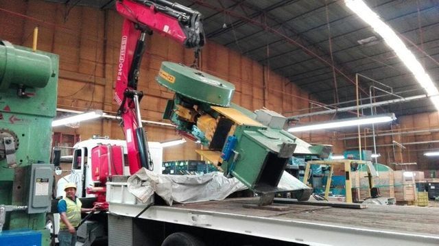 Una grúa levanta una máquina en un almacén.