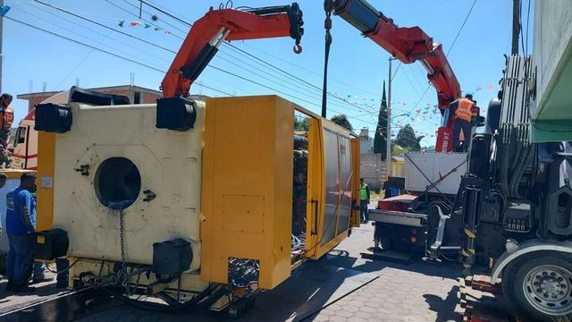 Una grúa levanta una gran caja amarilla.