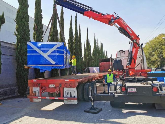 Una grúa levanta una gran caja azul en un remolque.