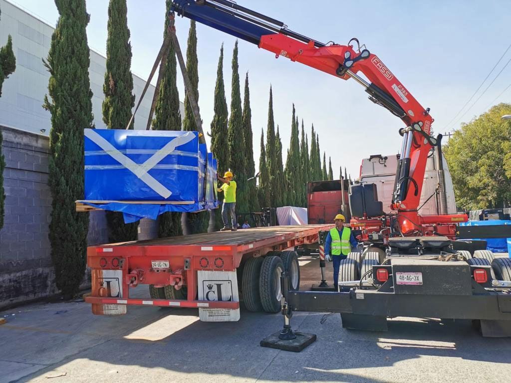 Una grúa levanta una gran caja azul en un remolque.