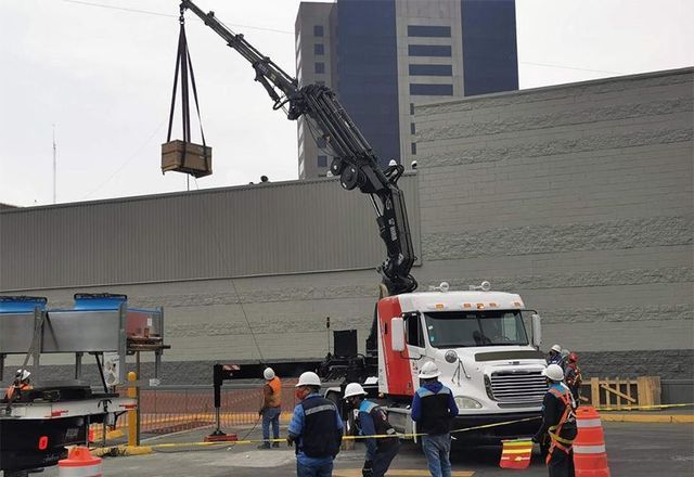 Una grúa levanta una caja desde la parte trasera de un camión
