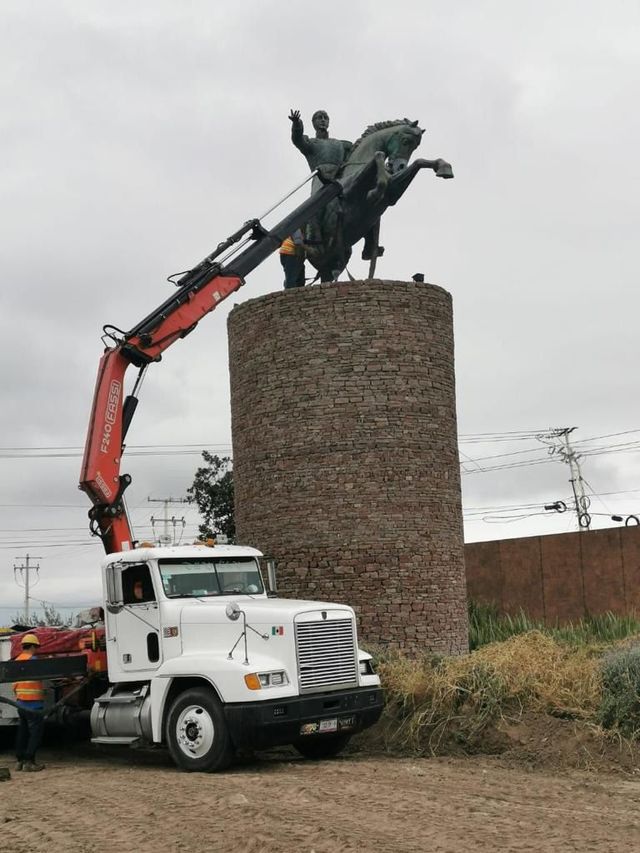 Una grúa levanta una estatua de un hombre a caballo