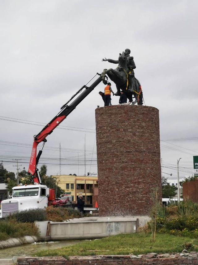 Una grúa levanta una estatua de un hombre a caballo