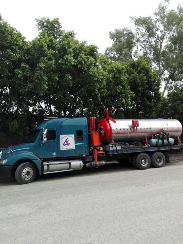 Un camión azul con un tanque rojo en la parte trasera está estacionado al costado de la carretera.