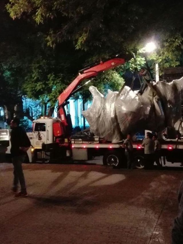 Un camión levanta una gran estatua por la noche