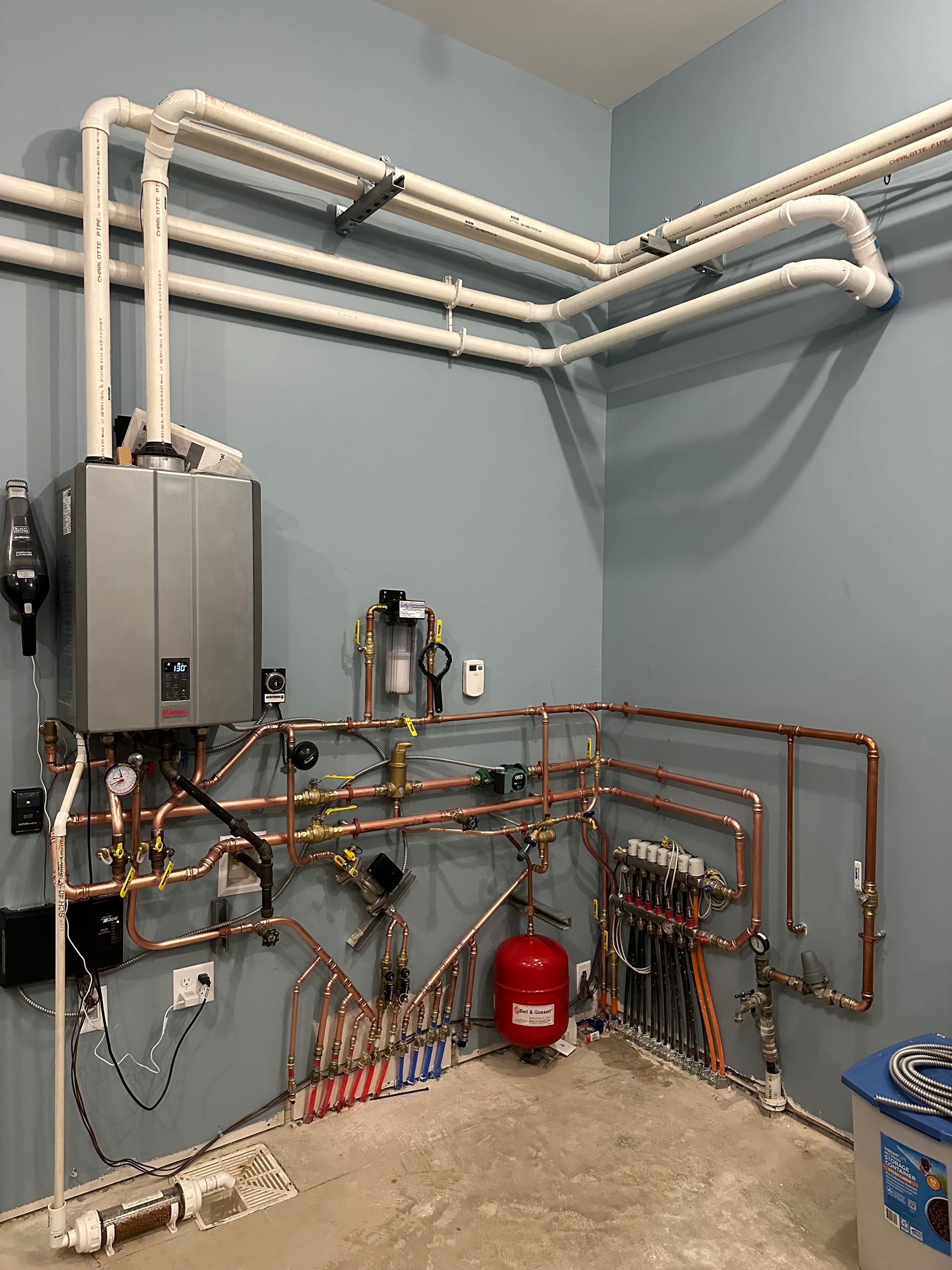 A room with a lot of pipes and a boiler on the wall.