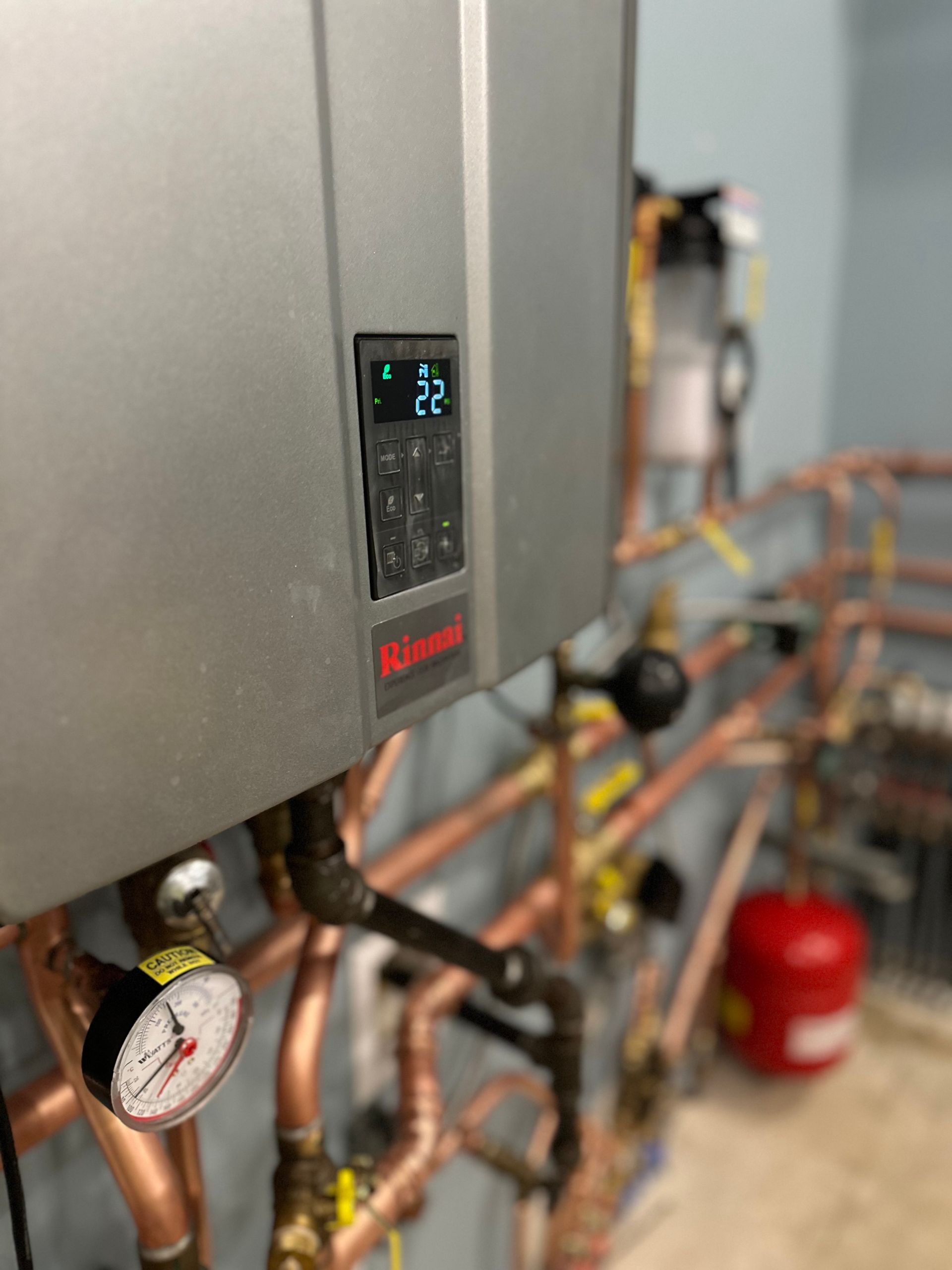 A close up of a water heater in a room with copper pipes.