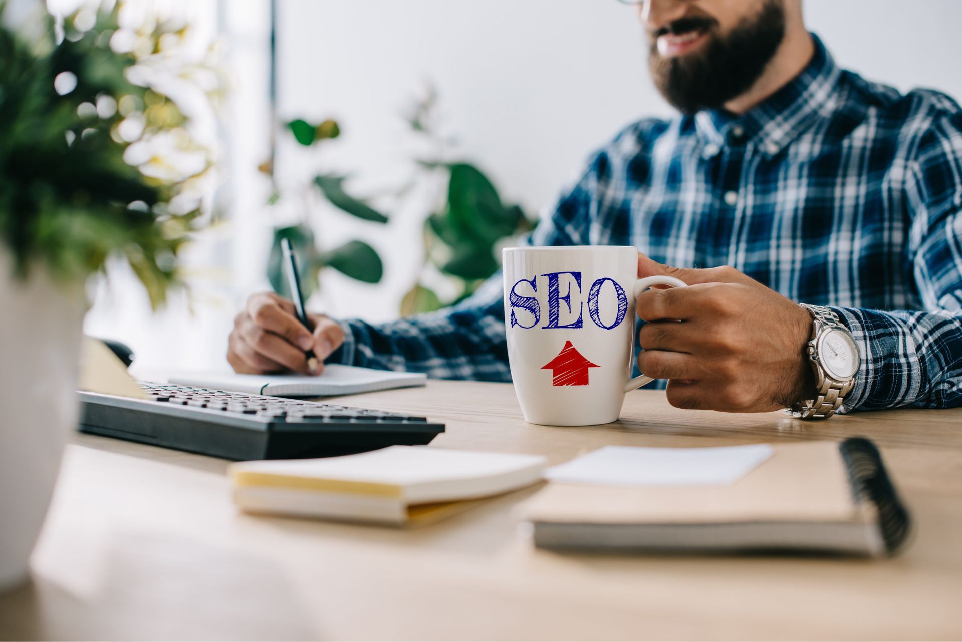 Professional sitting in front of a computer, writing notes while holding a mug with SEO printed on it, focused on digital marketing or search engine optimization tasks. Professional sitting in front of a computer, writing notes while holding a mug with SEO printed on it, focused on digital marketing or search engine optimization tasks.