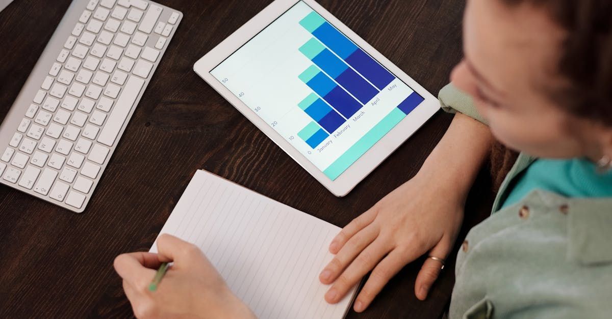 A professional viewing a graph on a tablet screen while writing notes on a sheet of paper. A professional viewing a graph on a tablet screen while writing notes on a sheet of paper.