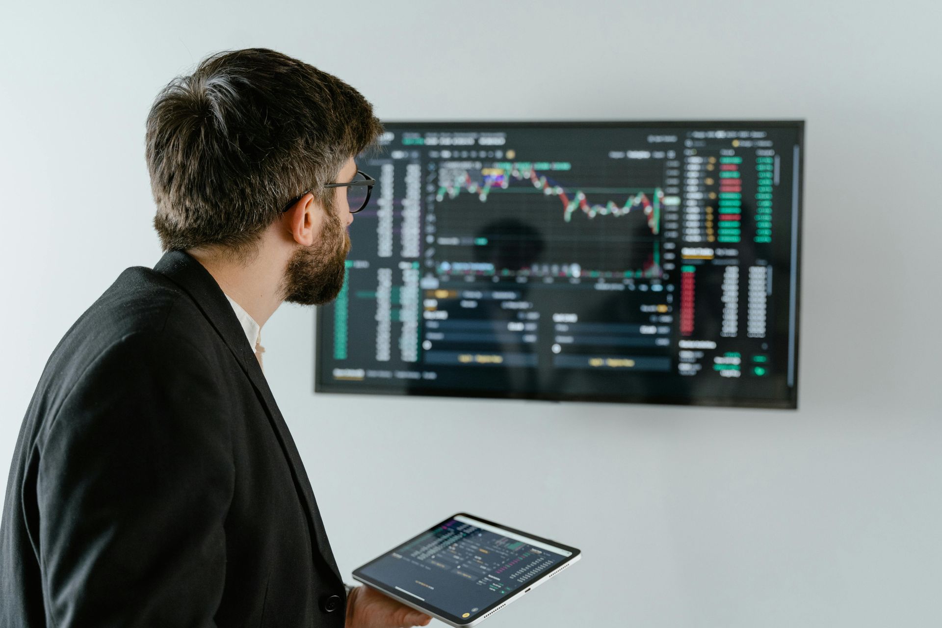 A professional looking at a monitor displaying marketing graphs while holding a tablet, analyzing data and performance metrics. A professional looking at a monitor displaying marketing graphs while holding a tablet, analyzing data and performance metrics.
