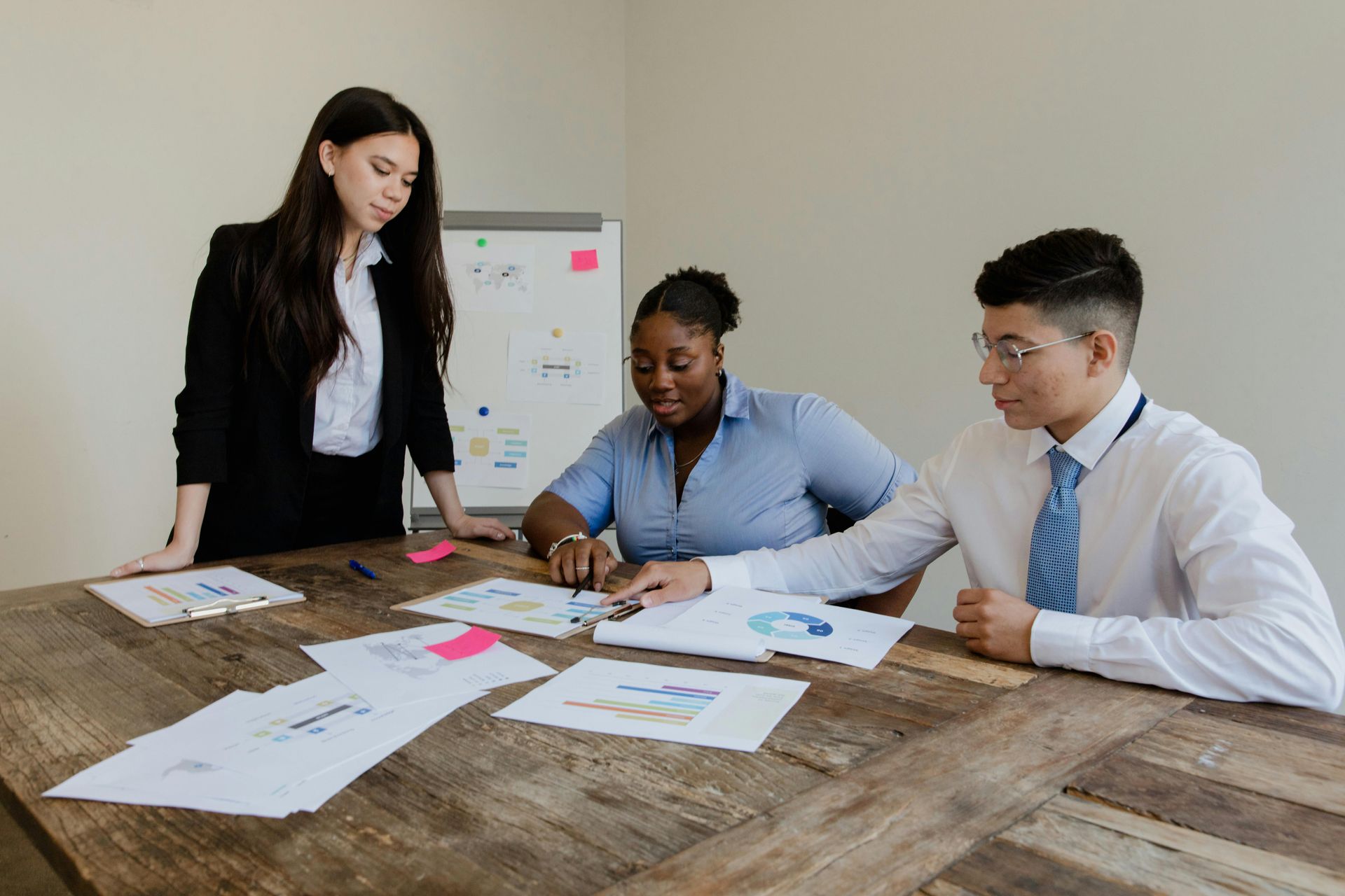 Three professionals sitting at a table, closely reviewing website printed graphs and charts Three professionals sitting at a table, closely reviewing website printed graphs and charts