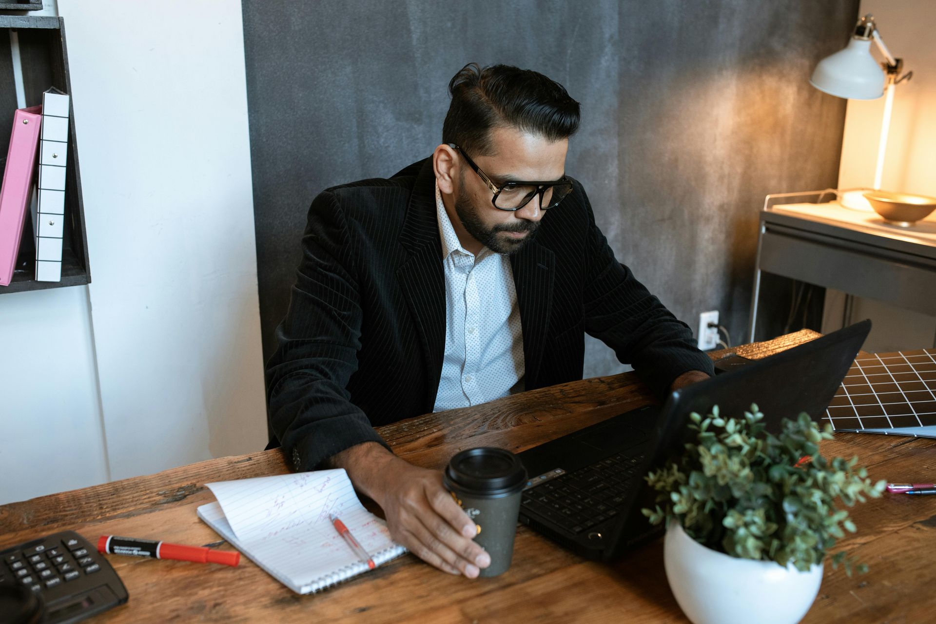 website design professional focused on a computer, holding a cup of coffee and notes on the side