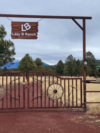 Wooden gate at Lazy B Ranch with a rustic sign and open ranch entrance under a blue sky