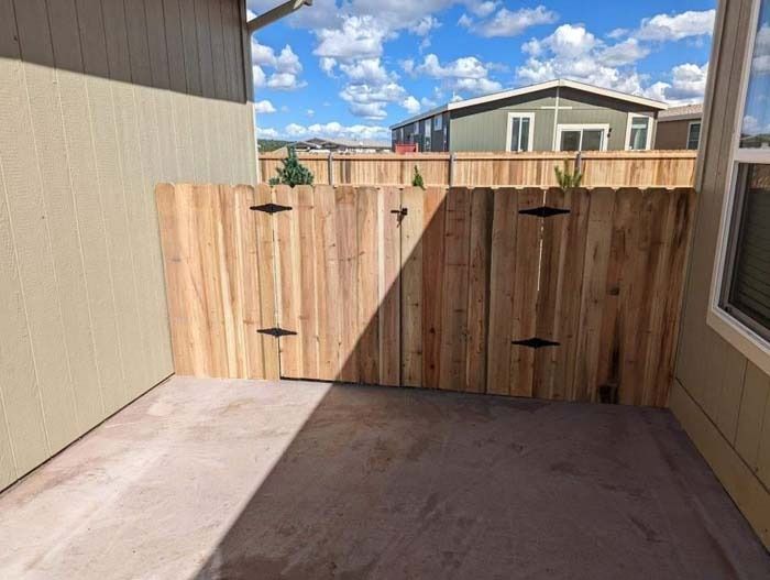 Wooden gate at the end of a narrow concrete patio between house walls, in bright sunlight.