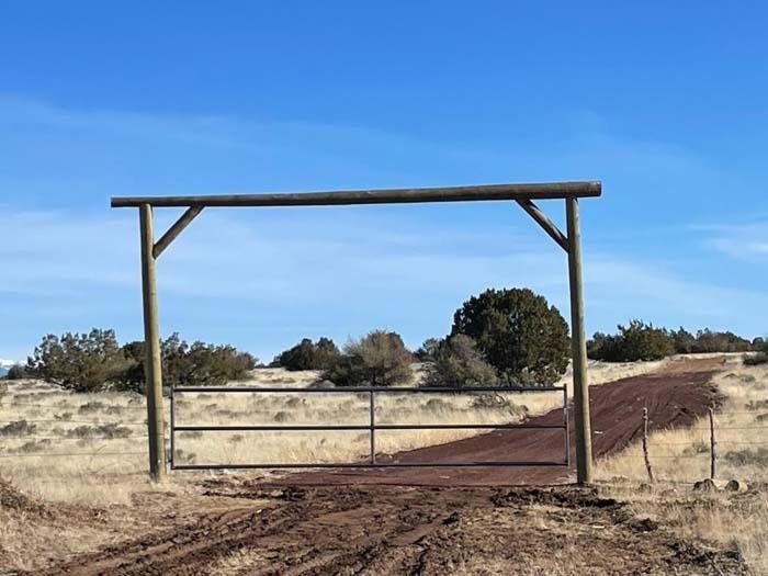 Rural dirt road entrance with a wooden gate under a blue sky