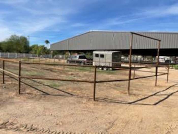 Empty dirt lot with fenced animal pens and a white trailer under a sunny blue sky
