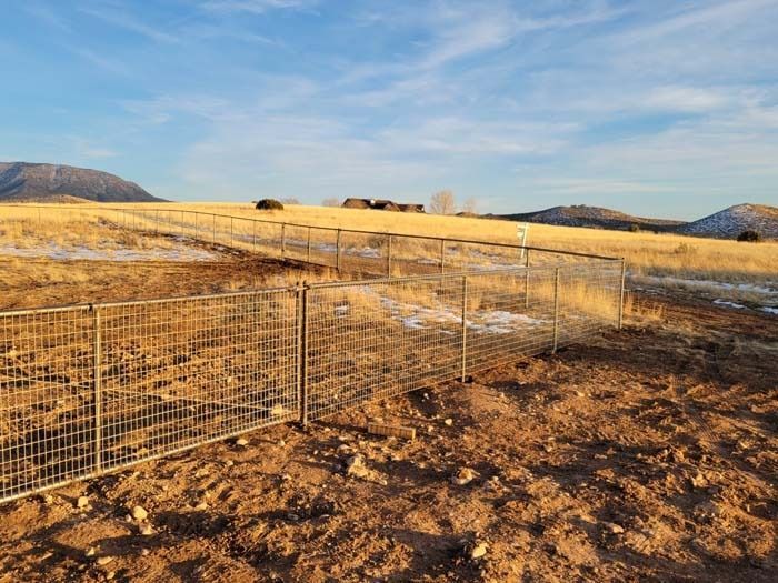Wire fence enclosure on a dry, rocky field with golden grass and distant hills under a blue sky.