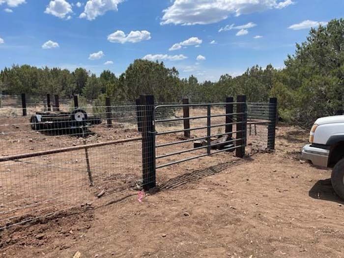 Rural dirt lot with black metal fence posts, a gate, and a white truck under a blue sky