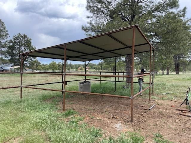 Rusty metal livestock shelter in a grassy field under cloudy sky