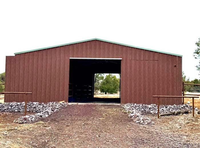 Brown metal barn with a large open doorway on a gravel lot