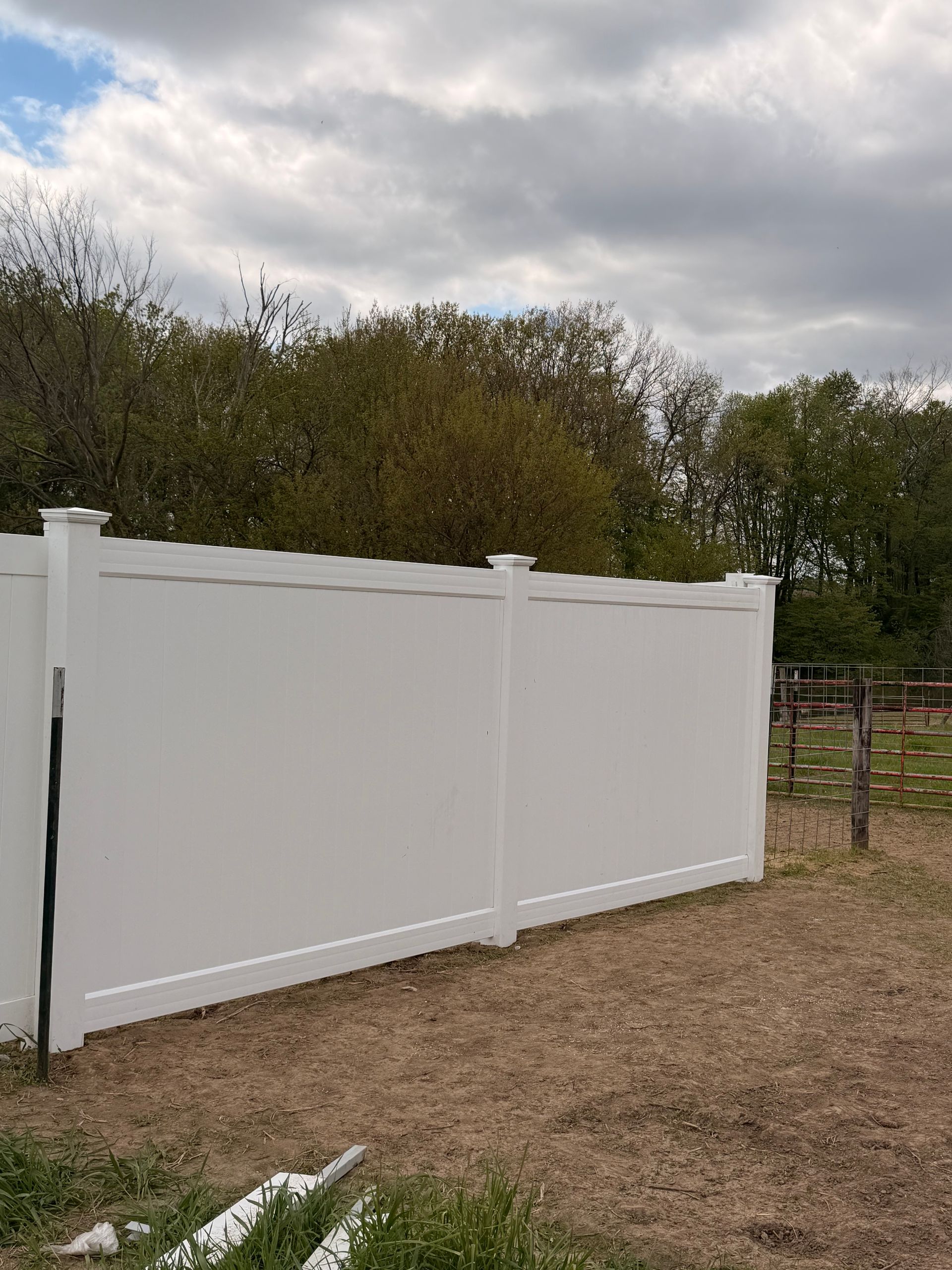 White vinyl fence along a gravel yard with trees and a cloudy sky behind it